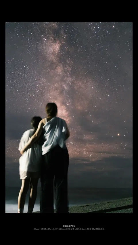 Two people under the Milky Way, in a black 9:16 frame